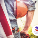 Man facing towards a field, holding a hard hat with tools in his back pocket and an American Flag draped over his shoulder. Happy Labor Day